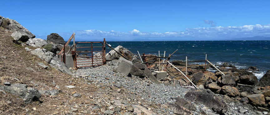 A rusty metal gate blocks access to a pebbly beach.