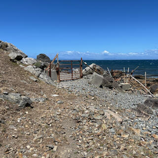 A rusty metal gate blocks access to a pebbly beach.