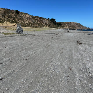 A vertical slab of stone on the left of a wide shingle beach.