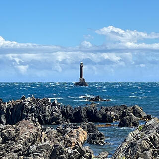 A tall structure in stormy sea beyond the rocky coastline.