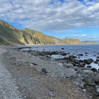A shingle coastline and distant hills illuminated by the sun.