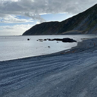 Grey clouds above a dark shingle beach and distant headland.