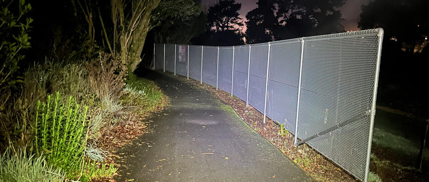 A tall chain link fence next to a narrow pathway.