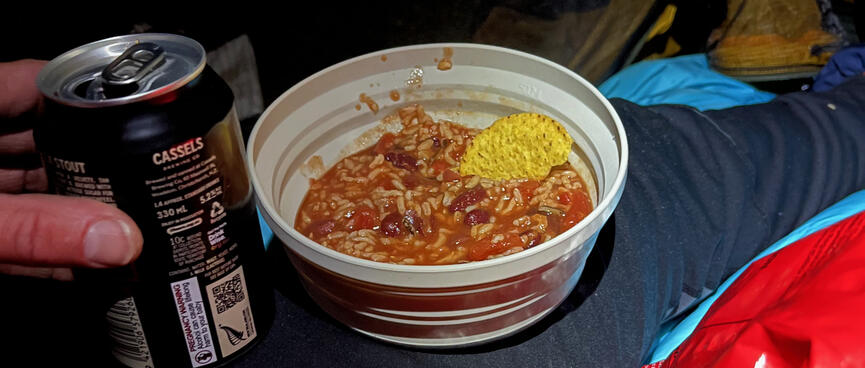 A can of Cassels beer and a collapsible camping bowl containing rice, beans and a nacho chip.