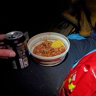 A can of Cassels beer and a collapsible camping bowl containing rice, beans and a nacho chip.