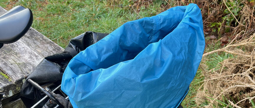A large blue sack folded over the edges of an Ortlieb pannier bag.