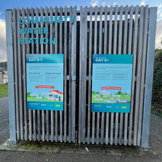 Signboards on a community water station explain that its purpose is to provide houses with water from day 8 onwards after a significant earthquake.