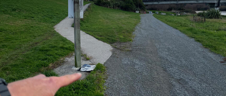 A cycleway sign lies on the ground next to a fork in the trail.