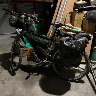 My loaded touring bike leans against a pile of boxes in a dark garage.