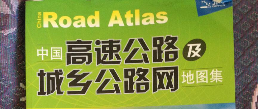 The soft cover of an atlas shows Chinese writing and pictures of empty highway.