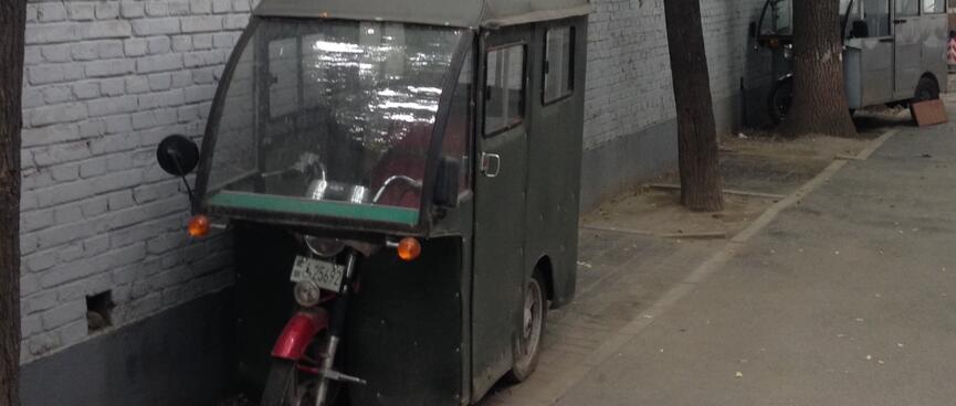 The front of a motorcycle protrudes from a glassed metal cab.
