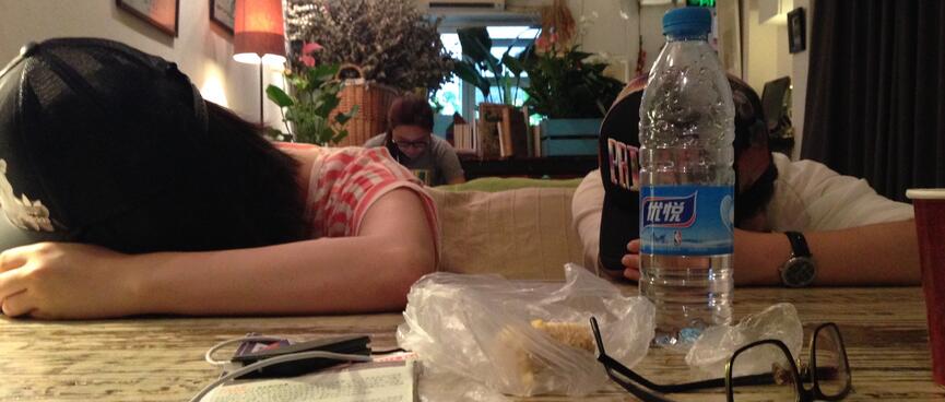Two young girls sleep on my table, by resting their heads on their arms.
