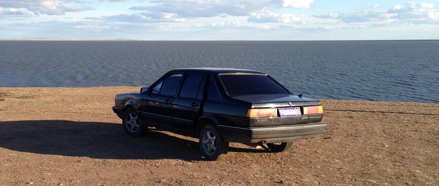A black car parked on a barren, elevated section of the shore.