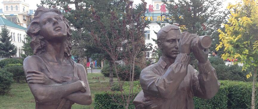 Statues of a young lady with arms folded and a man with a telescope.