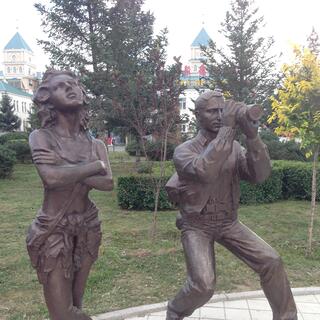 Statues of a young lady with arms folded and a man with a telescope.