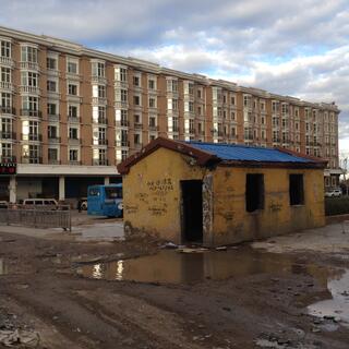 A large apartment block stands watch over a derelict shack covered in telephone numbers.