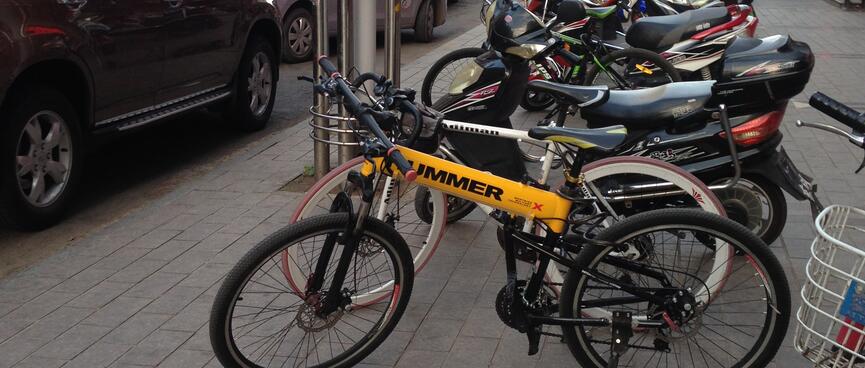 Bicycles and motorcycles are lined up on the footpath.