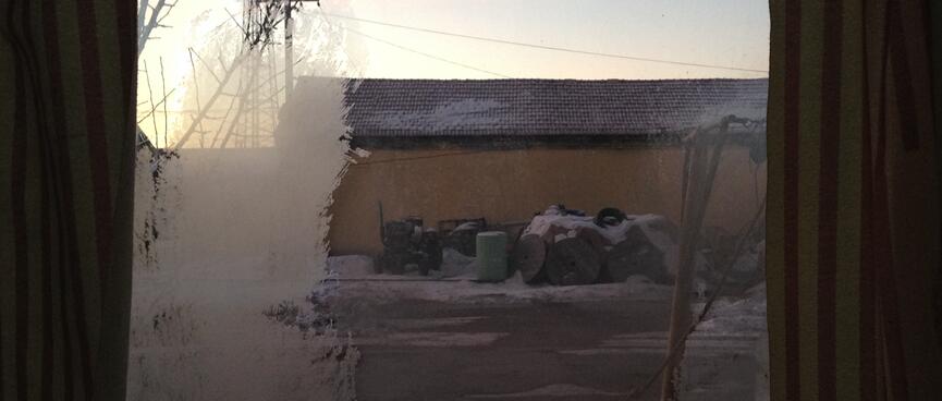 There is ice on the window, through which I can see blue sky and a tractor.
