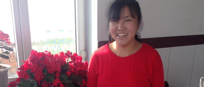 A woman wearing a red jumper stands next to a vase filled with red flowers.