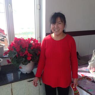 A woman wearing a red jumper stands next to a vase filled with red flowers.