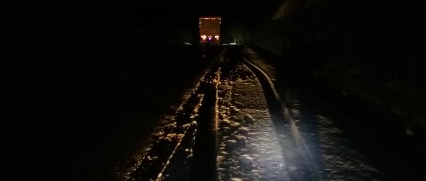 A carʼs headlights illuminate the snowy road ahead.