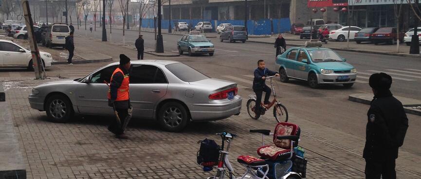 The boy on the bike is watched by a street cleaner and police man.