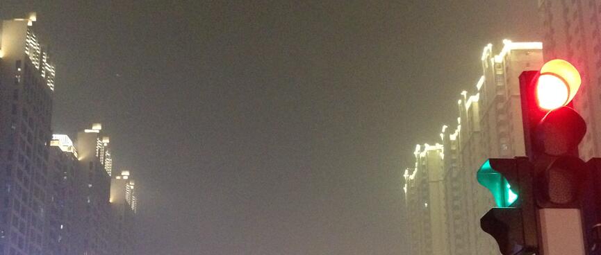A smog filled street flanked by iluminated high rises.