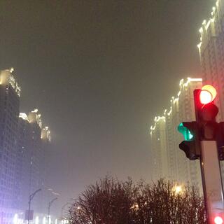 A smog filled street flanked by iluminated high rises.