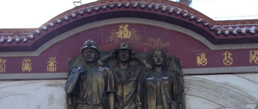 A life-size metal monument features two male miners in hardhats and a woman.