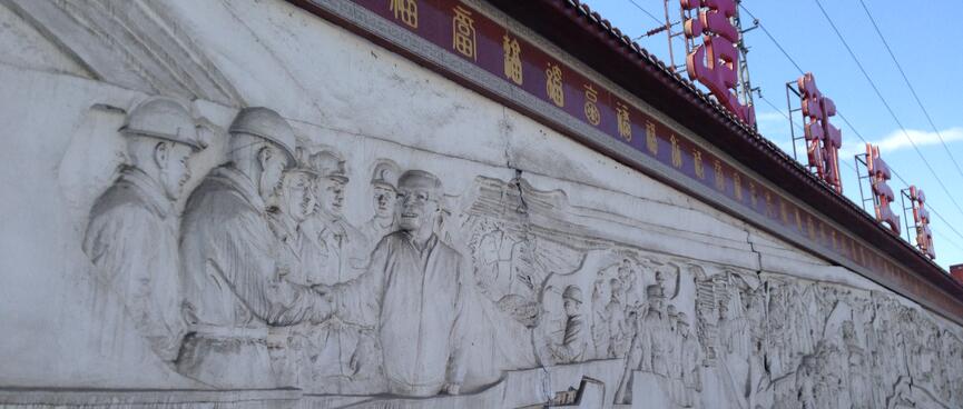 A mural carved in a stone wall features many miners and one shaking a manʼs hand.