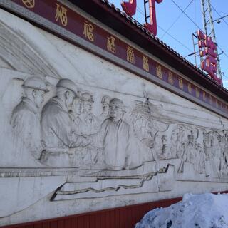 A mural carved in a stone wall features many miners and one shaking a manʼs hand.