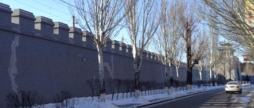A stone wall towers above a long straight road.