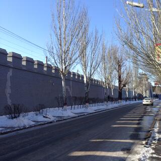 A stone wall towers above a long straight road.