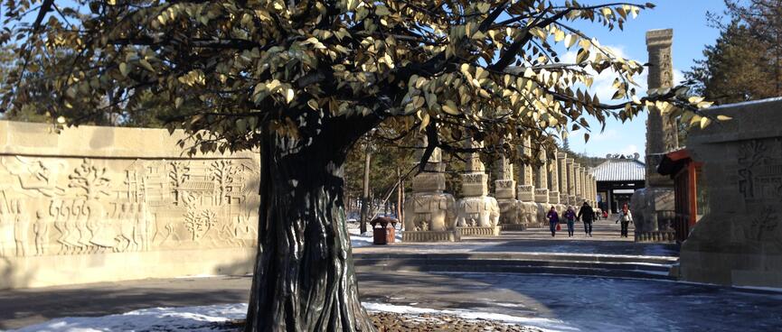 Pictures of trees are carved into a sandstone while a real or life-size tree stands nearby.