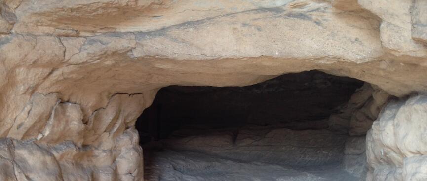 A wooden bridge leads to stone steps and a small hole in the rock.