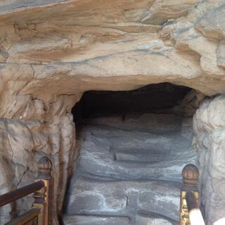 A wooden bridge leads to stone steps and a small hole in the rock.