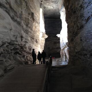 A tall narrow cavern where people view a huge carving bathed in a beam of light.