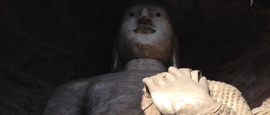 A huge carving of a standing buddha holding a cloak over its shoulder.