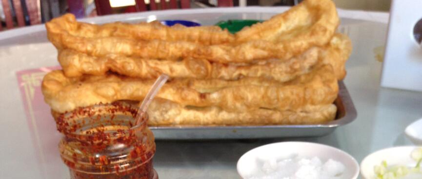 A bowl of noodle soup and a metal tray stacked with long golden fritters.