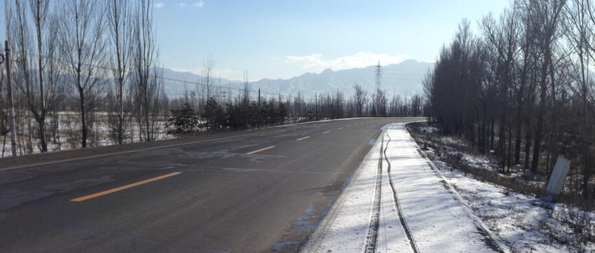 3 sets of tyre tracks in shallow snow on the roadʼs shoulder.