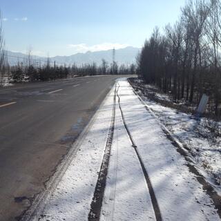 3 sets of tyre tracks in shallow snow on the road's shoulder.