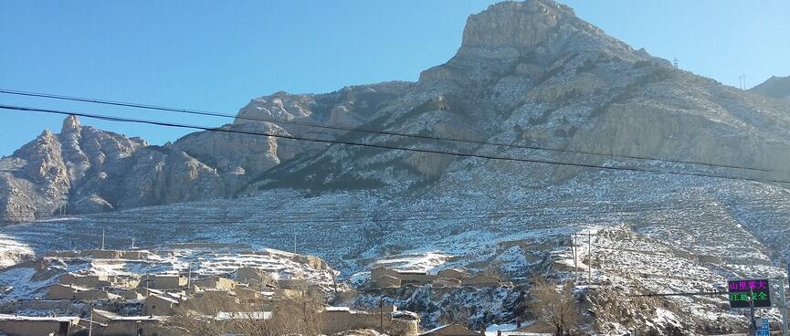 Buildings with rough rocky shapes sit at the foot of a large rocky mountain.