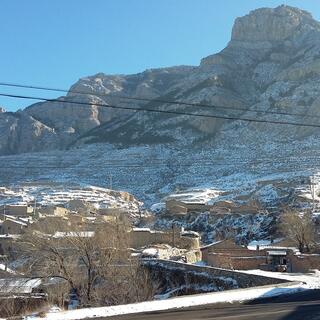 Buildings with rough rocky shapes sit at the foot of a large rocky mountain.