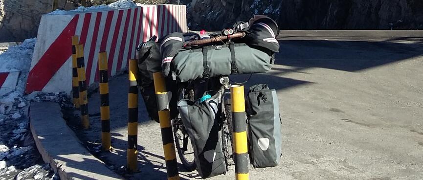 My bicycle leans agains poles on the road side, while rocky mountain cliffs line the road.