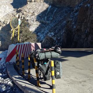 My bicycle leans agains poles on the road side, while rocky mountain cliffs line the road.