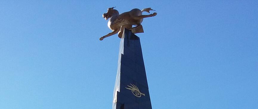 A tall pyramid emblazoned with Chinese lettering is topped by a statue of a running animal.