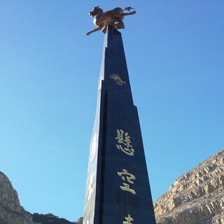 A tall pyramid emblazoned with Chinese lettering is topped by a statue of a running animal.