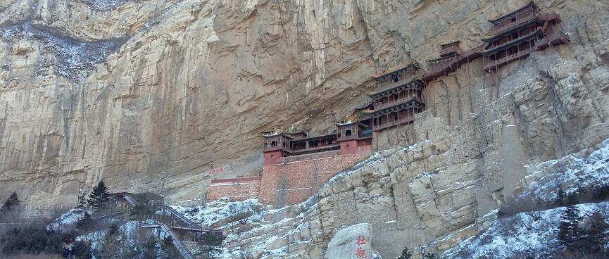 Several old wooden buildings protrude from a tall cliff face.