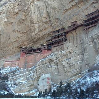 Several old wooden buildings protrude from a tall cliff face