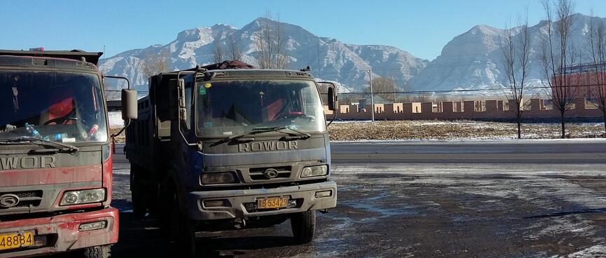 Two dirty trucks feature against a backdrop of snow dusted mountains.